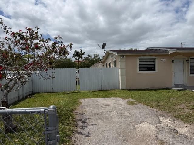 Stucco exterior featuring a dual-gate white vinyl privacy fence, horizontal sliding windows, and a paved driveway