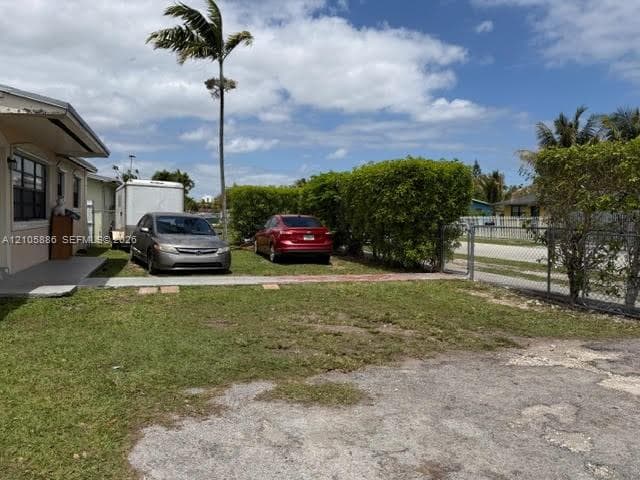 Property exterior featuring a concrete walkway, chain-link perimeter fencing, and mature hedge landscaping