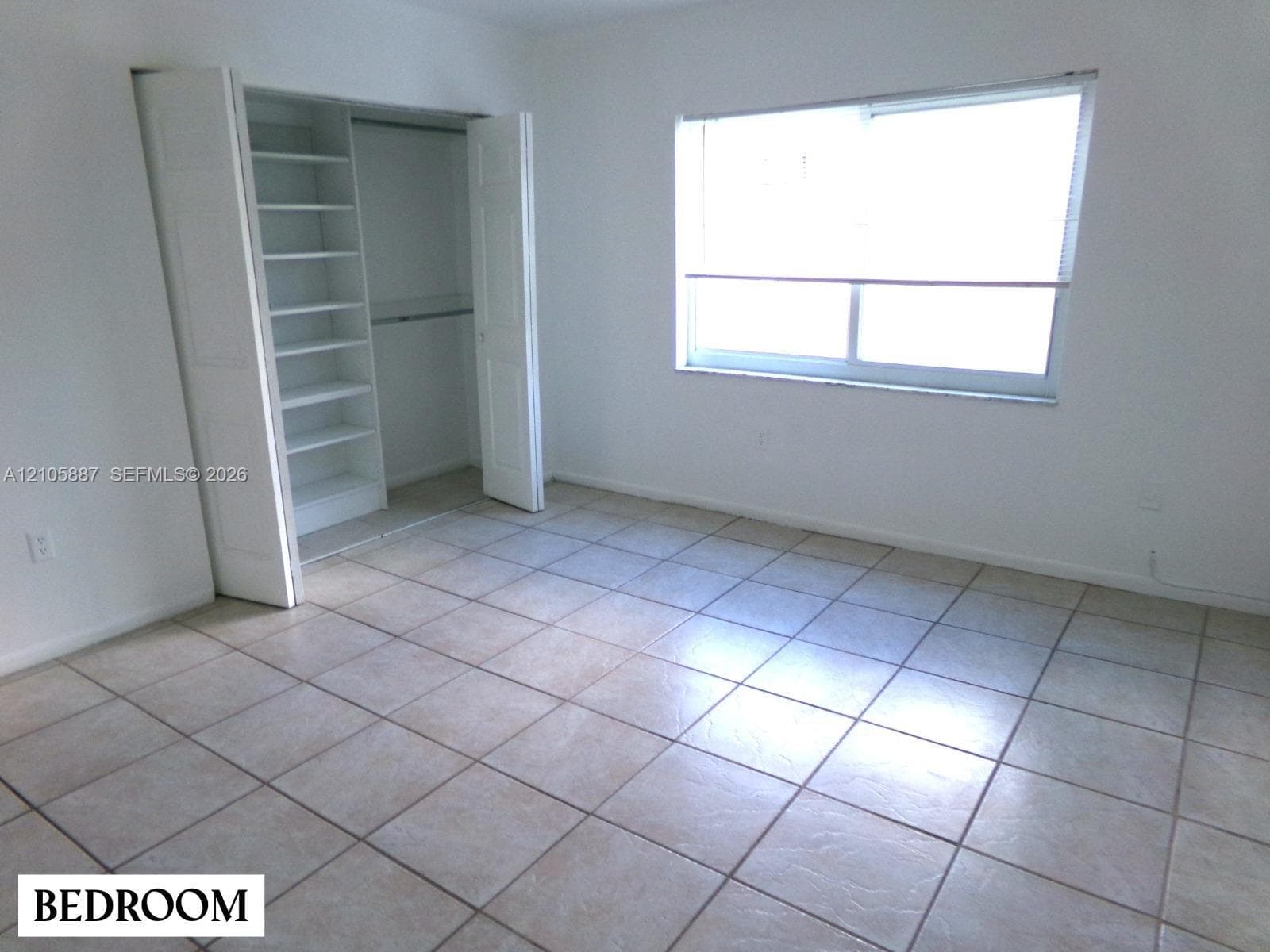 Neutral ceramic tile flooring, horizontal sliding window, and closet featuring integrated built-in shelving
