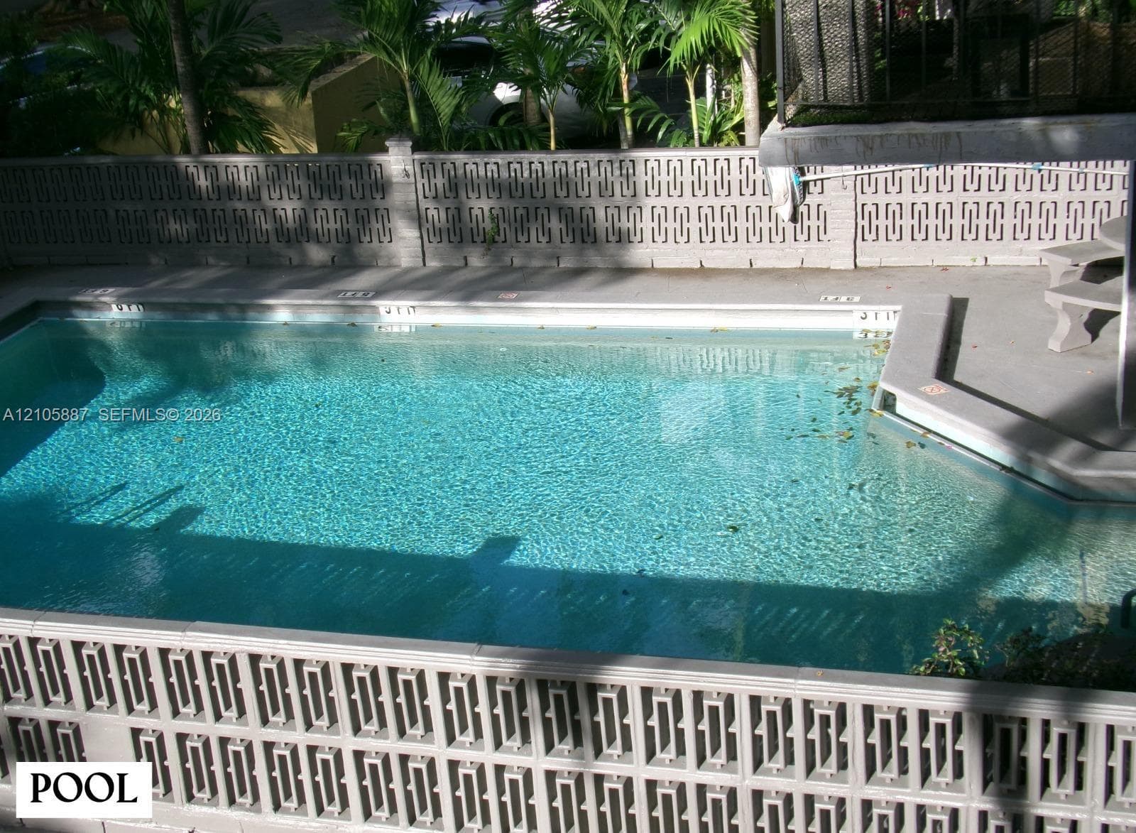 Inground pool featuring a concrete deck, built-in stone bench, and geometric breeze block perimeter fencing