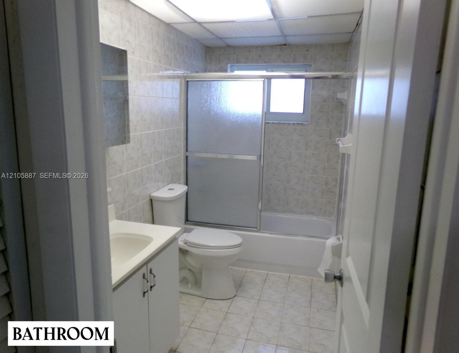 Bathroom featuring ceramic tile flooring, full-wall tiling, a vanity with an integrated basin, and a tub-shower combination enclosed by sliding glass doors