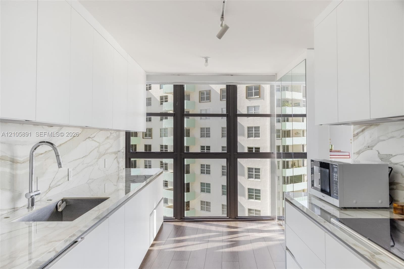 Kitchen featuring white flat-panel cabinetry, floor-to-ceiling windows, veined stone-finish countertops and backsplash, wood-finish flooring, and a stainless steel undermount sink with a gooseneck faucet