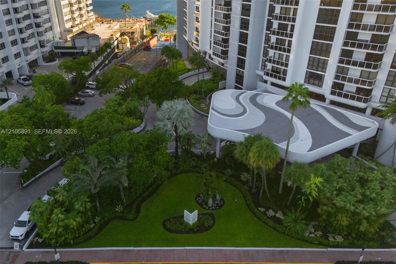 High-rise exterior featuring a patterned porte-cochère, manicured landscaping, mature trees, and paved motor court