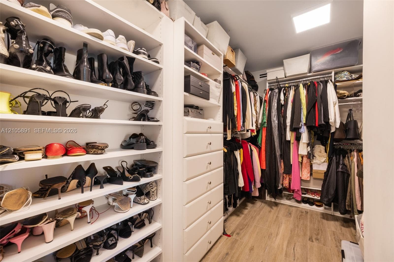 Custom dressing room featuring floor-to-ceiling adjustable shelving, integrated cabinetry with six soft-close drawers, dual-level hanging rods, and wood-finish flooring