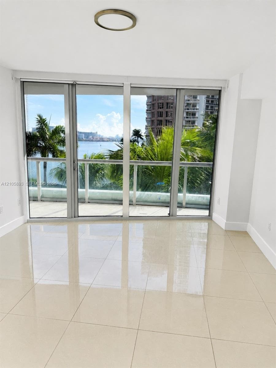 Large-format tile flooring, floor-to-ceiling glass sliding doors, private balcony with metal railing, and flush-mount circular ceiling lighting