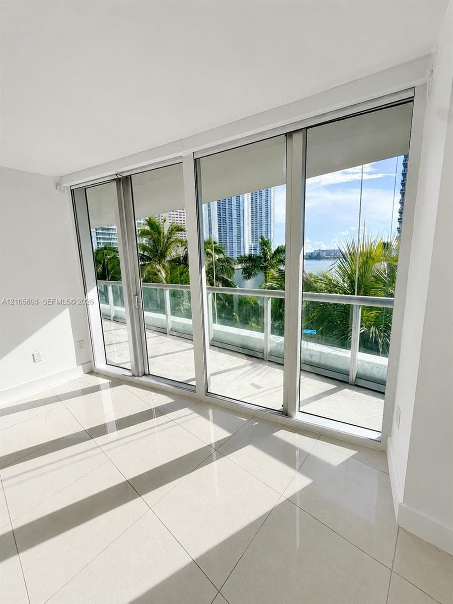 Floor-to-ceiling sliding glass doors, balcony with glass railing, large-format tile flooring, and neutral wall finishes