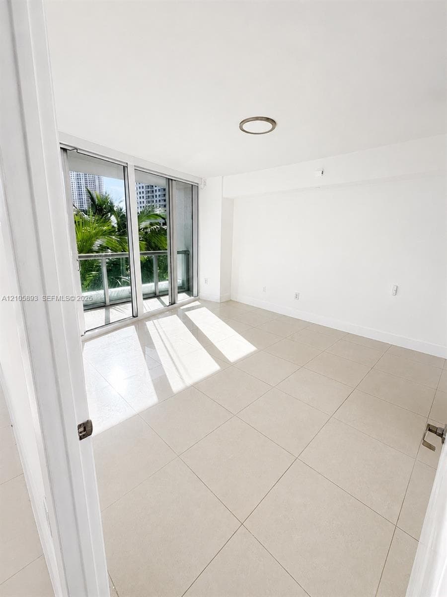 Interior space featuring large-format tile flooring, flush-mount circular lighting, and floor-to-ceiling glass sliding doors opening to an exterior balcony with a metal railing