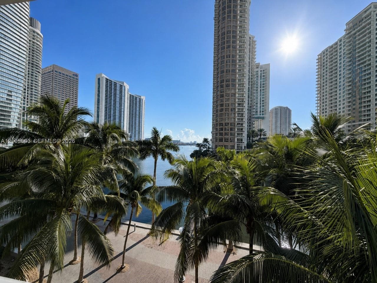 Waterfront terrace featuring stone paver flooring and mature palm trees, oriented toward urban high-rise skyline scenery