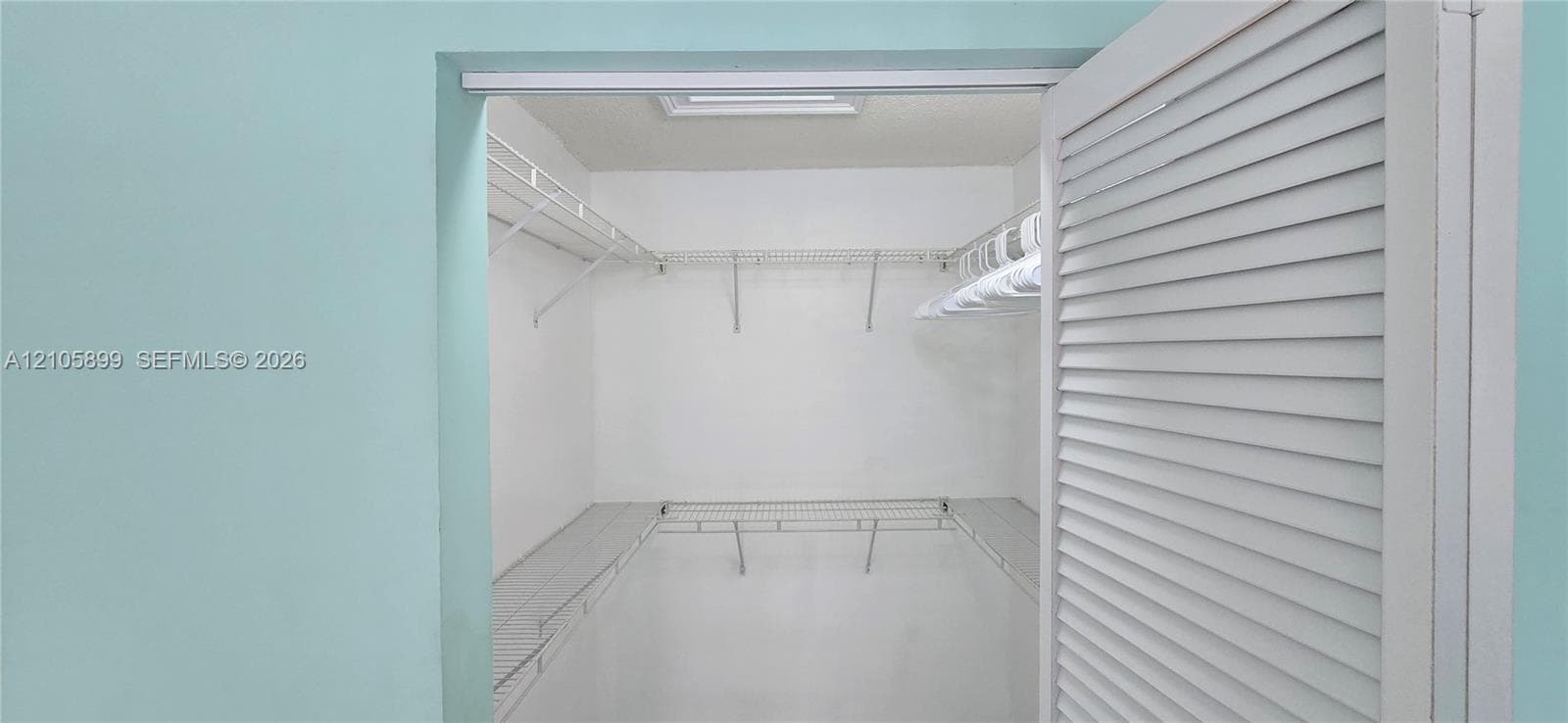 Walk-in closet featuring white louvered doors, white wire shelving, and a built-in ceiling light fixture