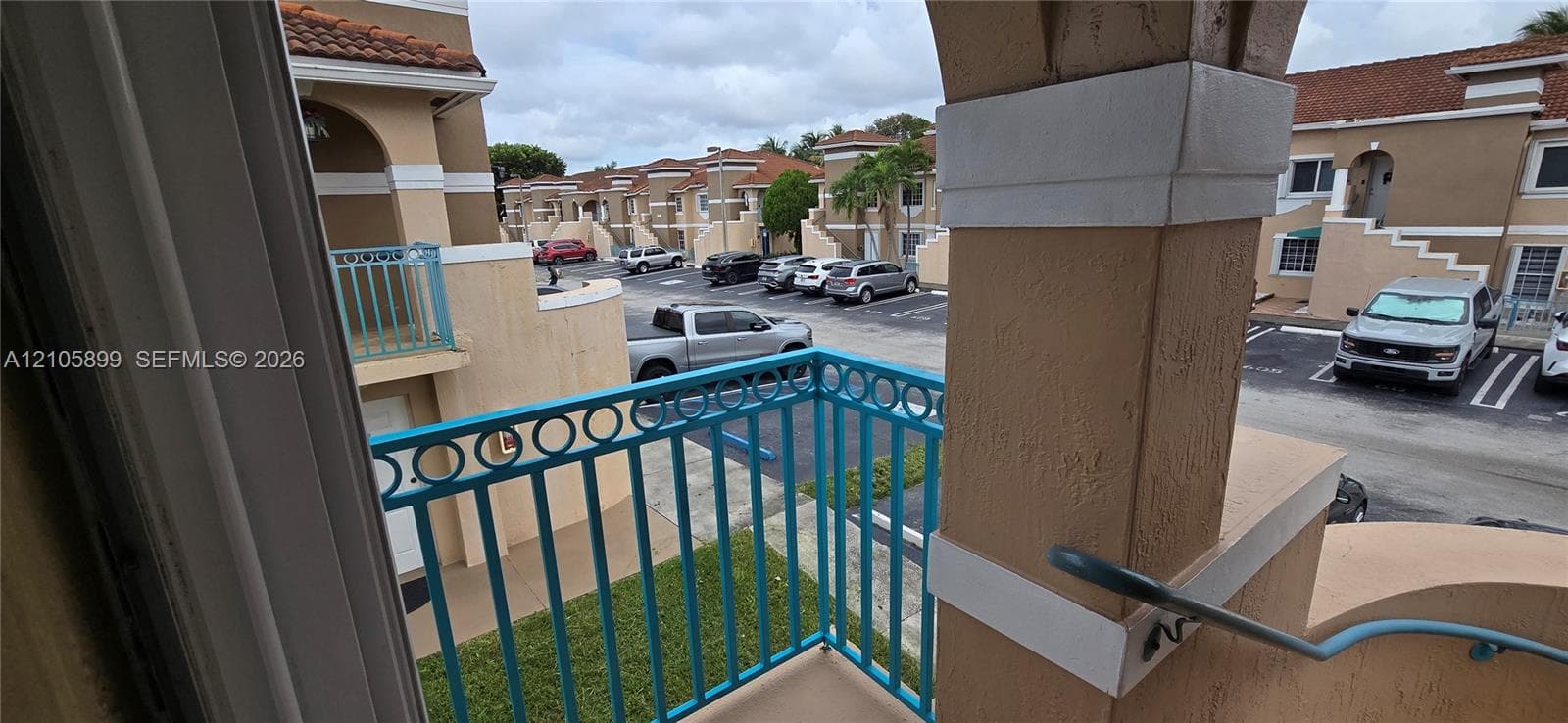 Balcony featuring blue metal railings, a stucco support pillar, and concrete flooring