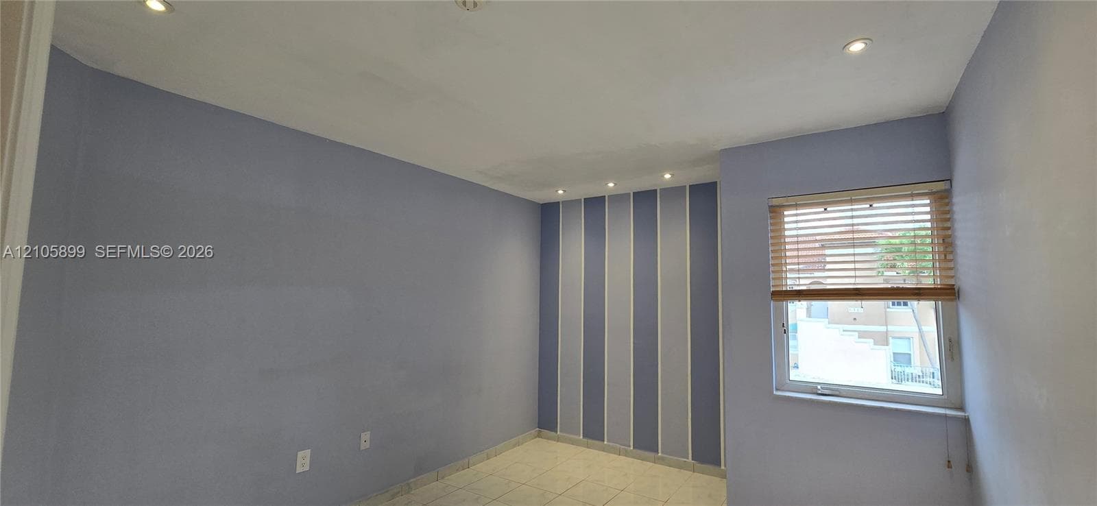Interior room featuring recessed ceiling lighting, a decorative vertical-striped accent wall, tile flooring, and a window equipped with wood-finish blinds
