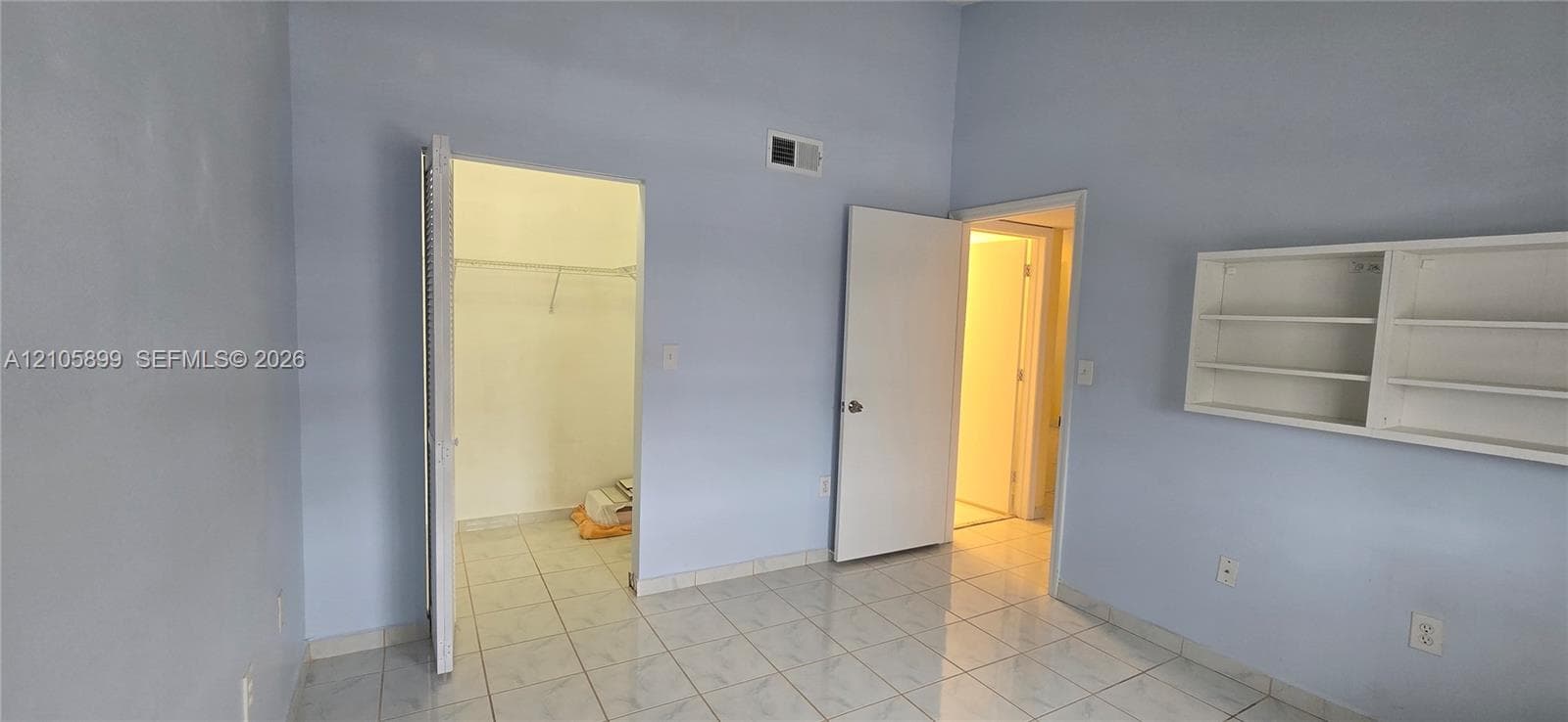 Room featuring light-colored tile flooring, built-in wall shelving, and a walk-in closet with integrated hanging rods