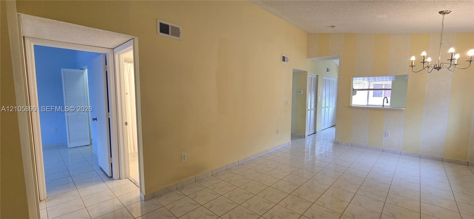 Interior space featuring light-colored tile flooring, arched wall cutouts, a dining area chandelier, and multiple doorway entries