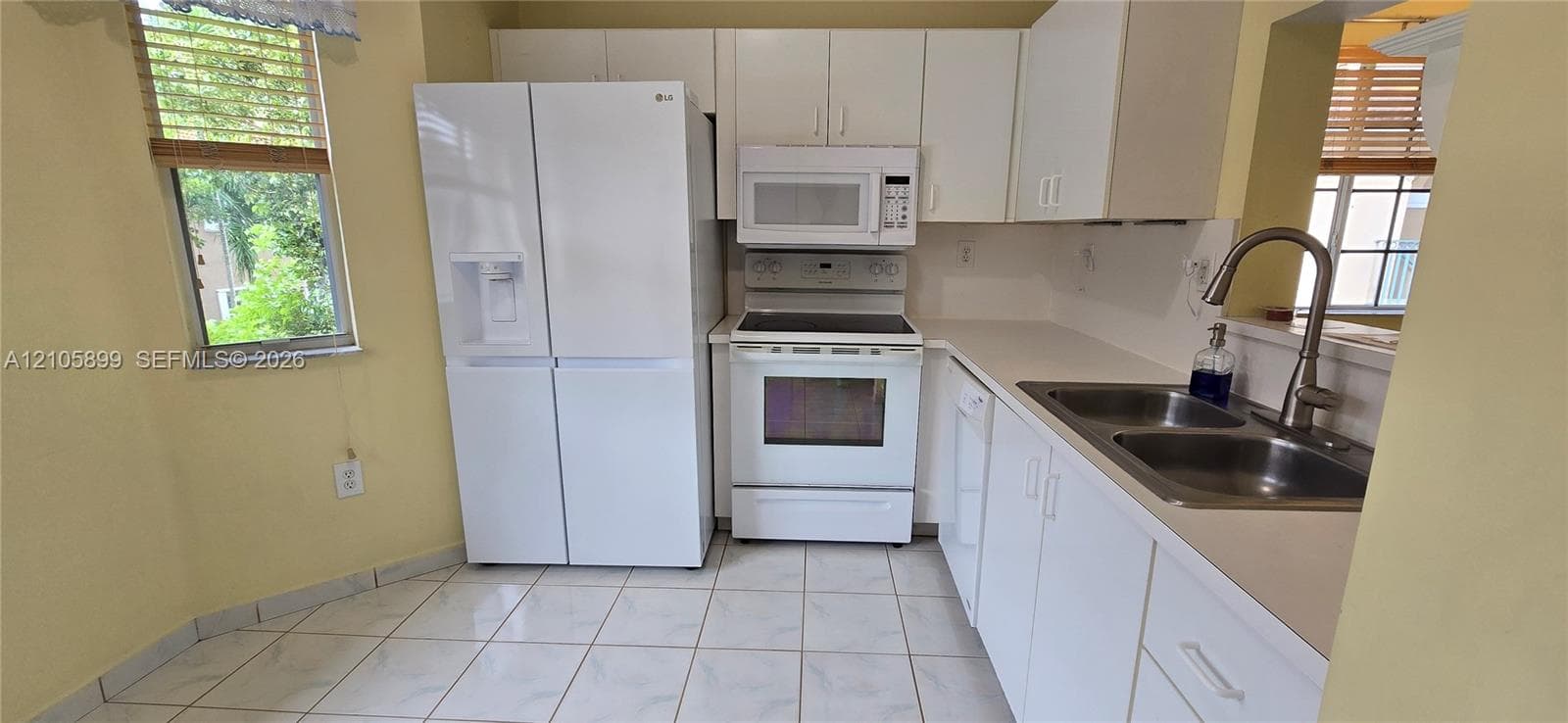 Kitchen featuring white cabinetry, a dual-basin stainless steel sink with a high-arc pull-down faucet, white appliance suite, and tile flooring