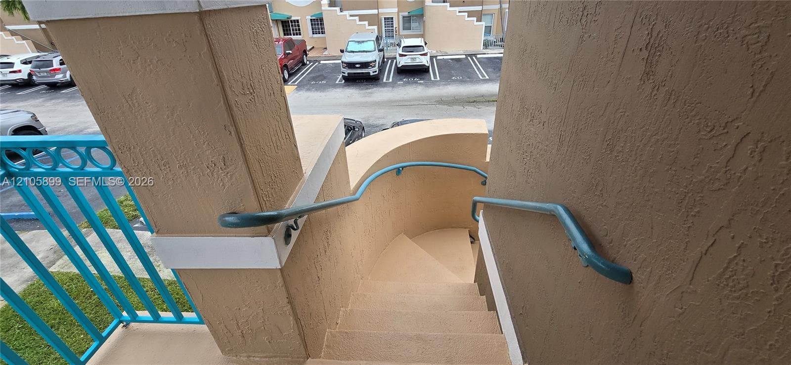 Stucco staircase featuring curved concrete steps, teal metal railings, and textured wall finishes