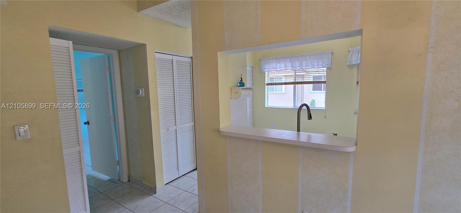 Pass-through window with a ledge, white louvered closet doors, and tile flooring