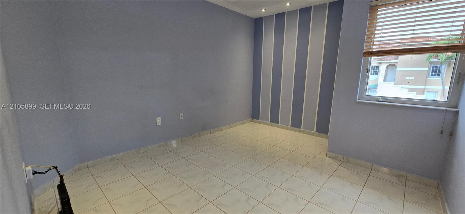 Room featuring neutral tile flooring, recessed ceiling lighting, a single window with horizontal blinds, and a striped accent wall
