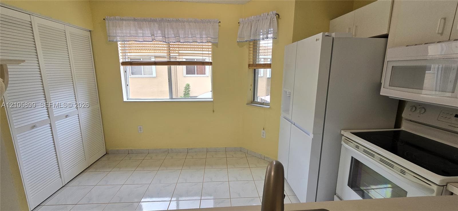 Kitchen featuring white ceramic tile flooring, built-in louvered-door cabinetry, and an integrated appliance suite including a white refrigerator and over-the-range microwave