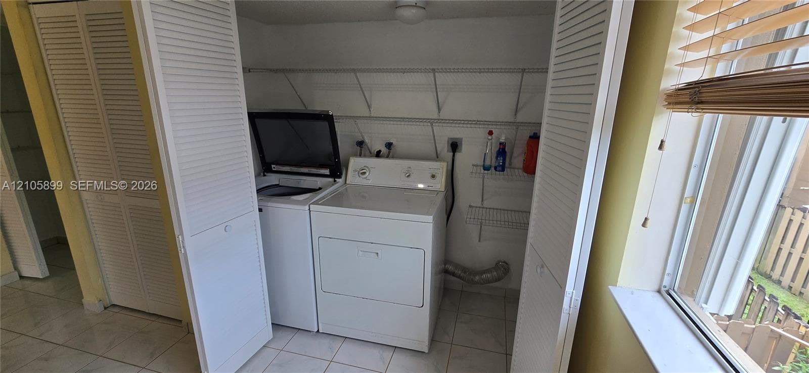 Laundry closet featuring white louvered bifold doors, tile flooring, and integrated metal wire shelving