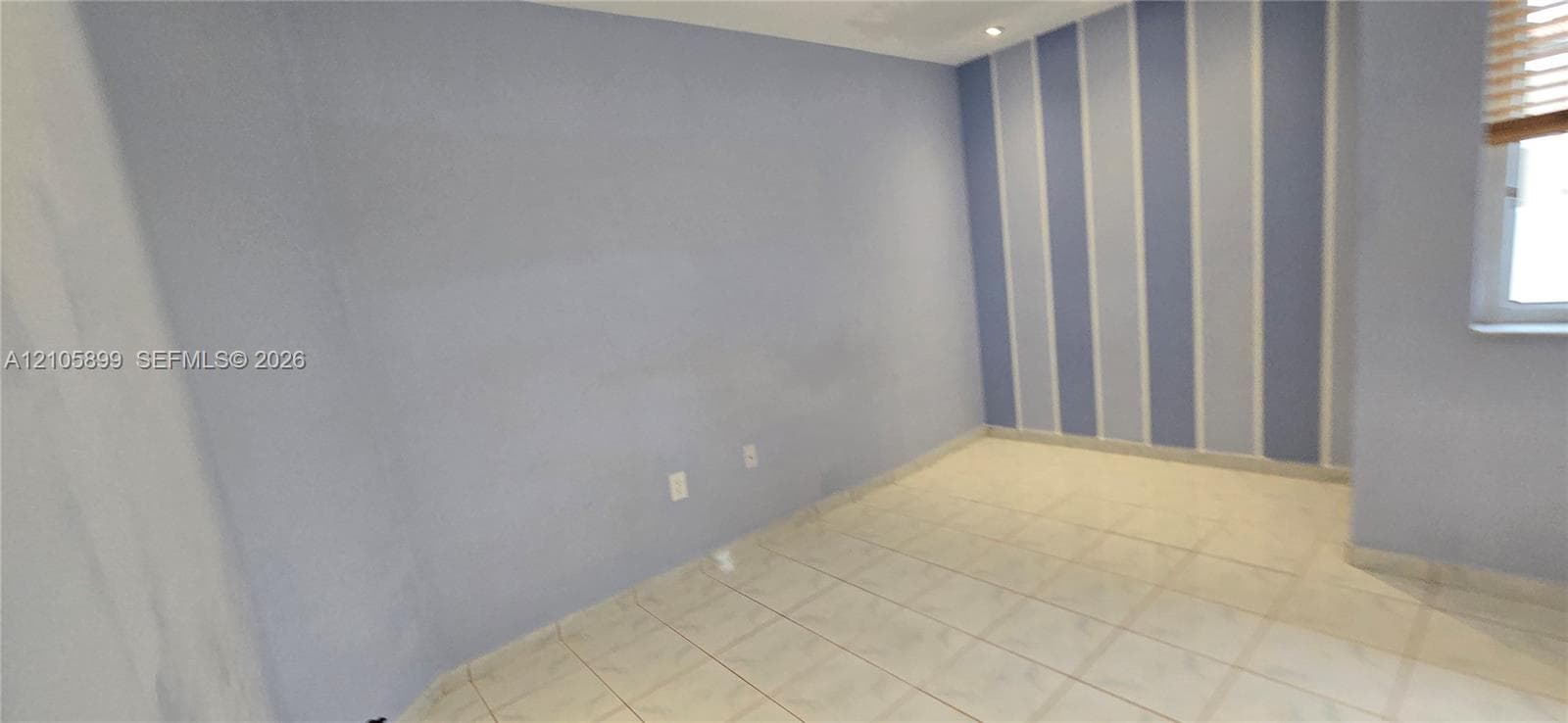 Room featuring light-toned tile flooring, recessed ceiling lighting, and a vertical stripe accent wall