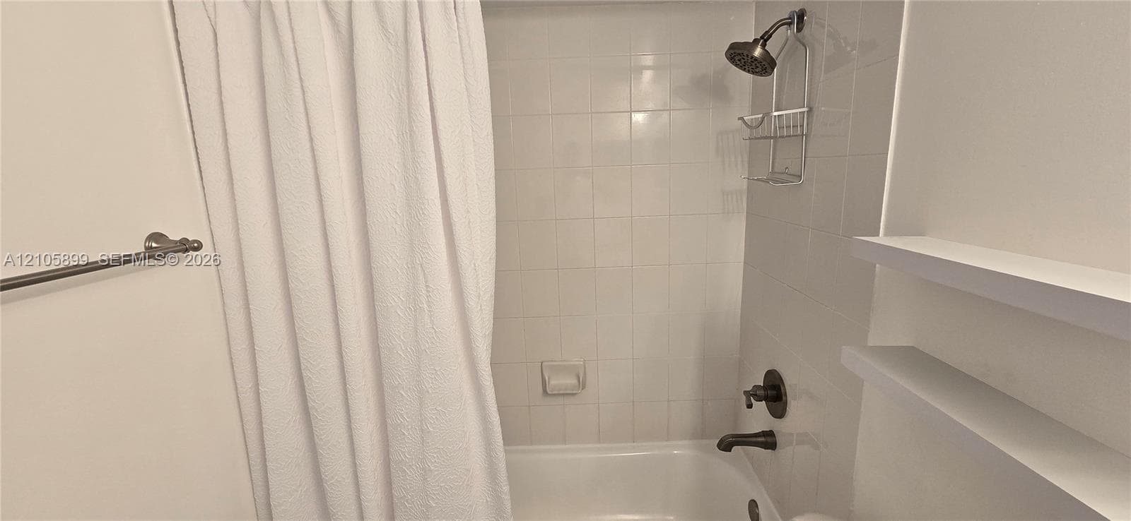 Bathtub surround featuring white square ceramic wall tiling, oil-rubbed bronze plumbing fixtures, and dual integrated floating shelves