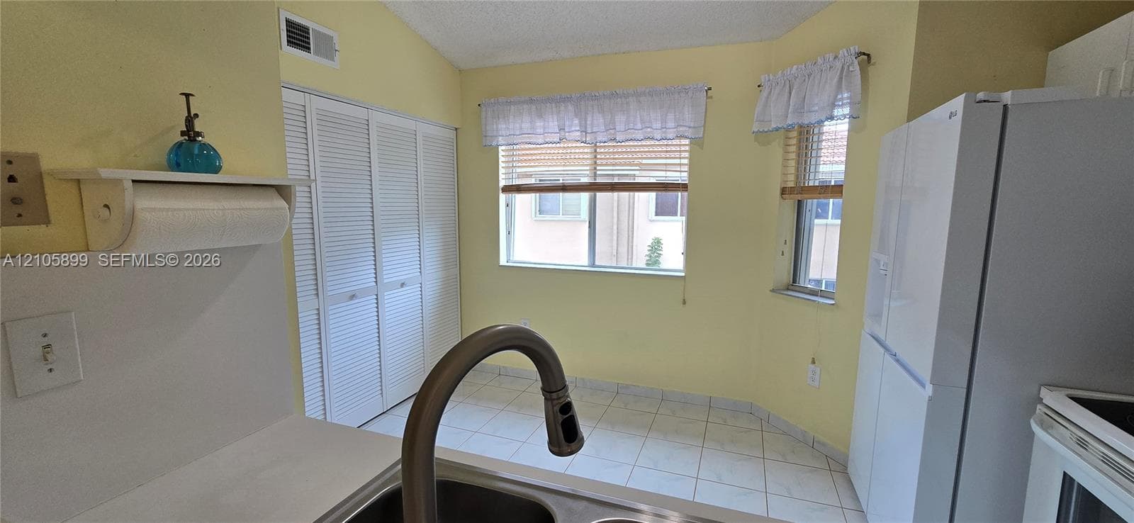 Kitchen featuring tile flooring, louvered-panel closet doors, vaulted ceiling, and dual windows with blinds