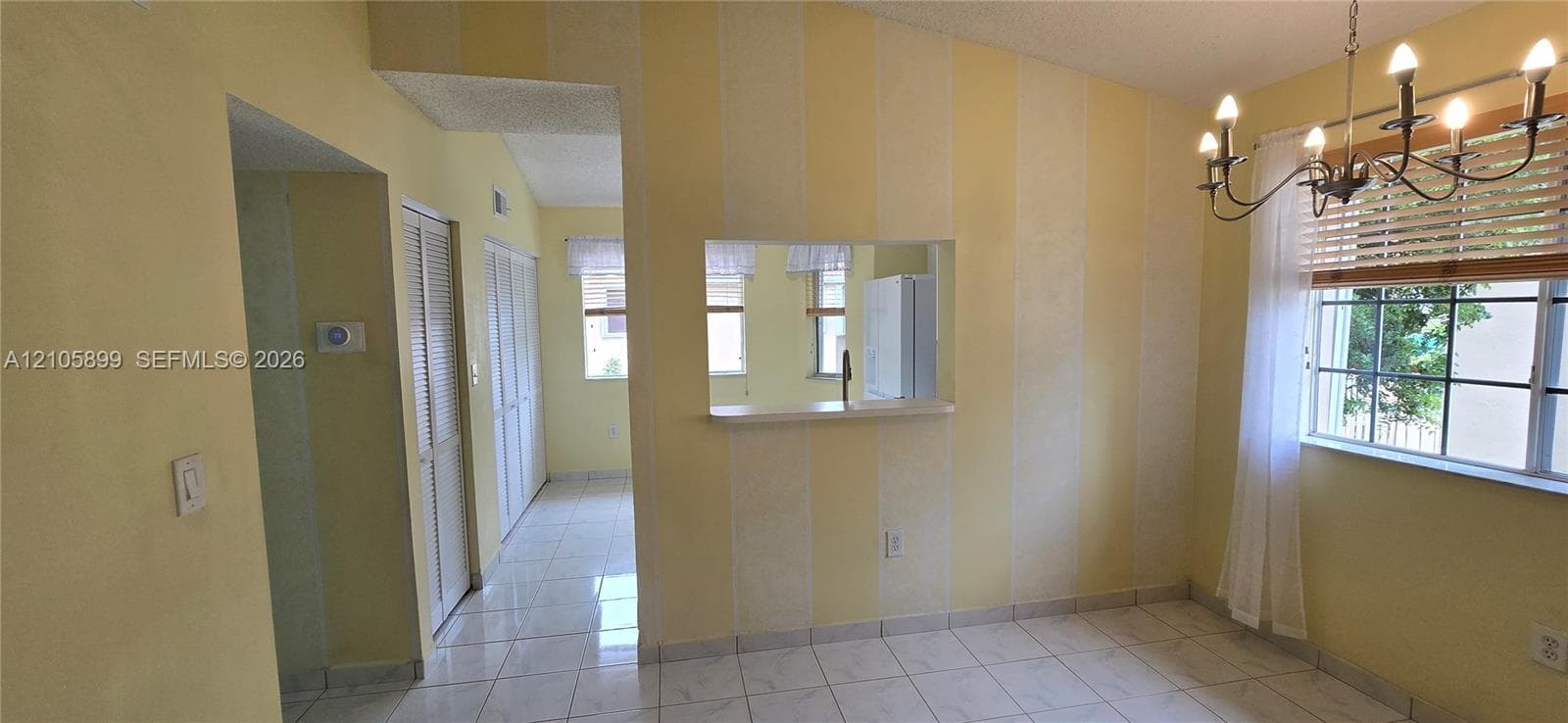 Dining area featuring ceramic tile flooring, a multi-arm chandelier, louvered closet doors, and a pass-through opening