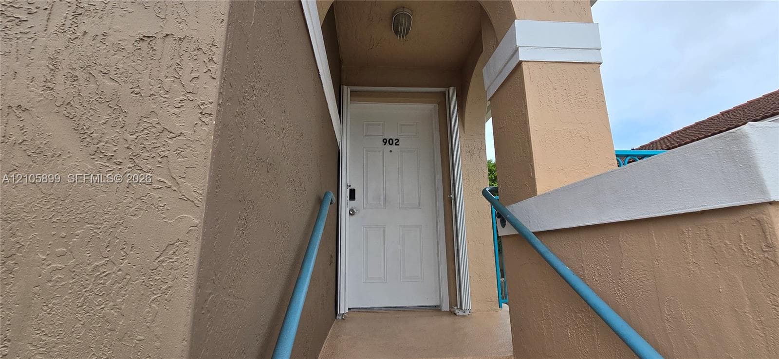 Covered entryway featuring a textured stucco exterior, a six-panel front door, and metal handrails