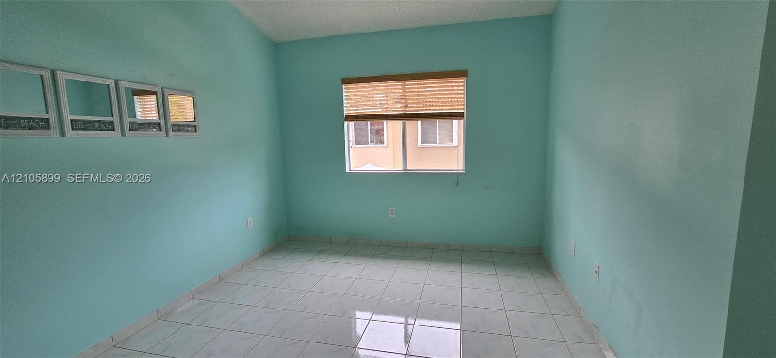 Interior room featuring white tile flooring, painted walls, and a window with a woven wood-finish blind
