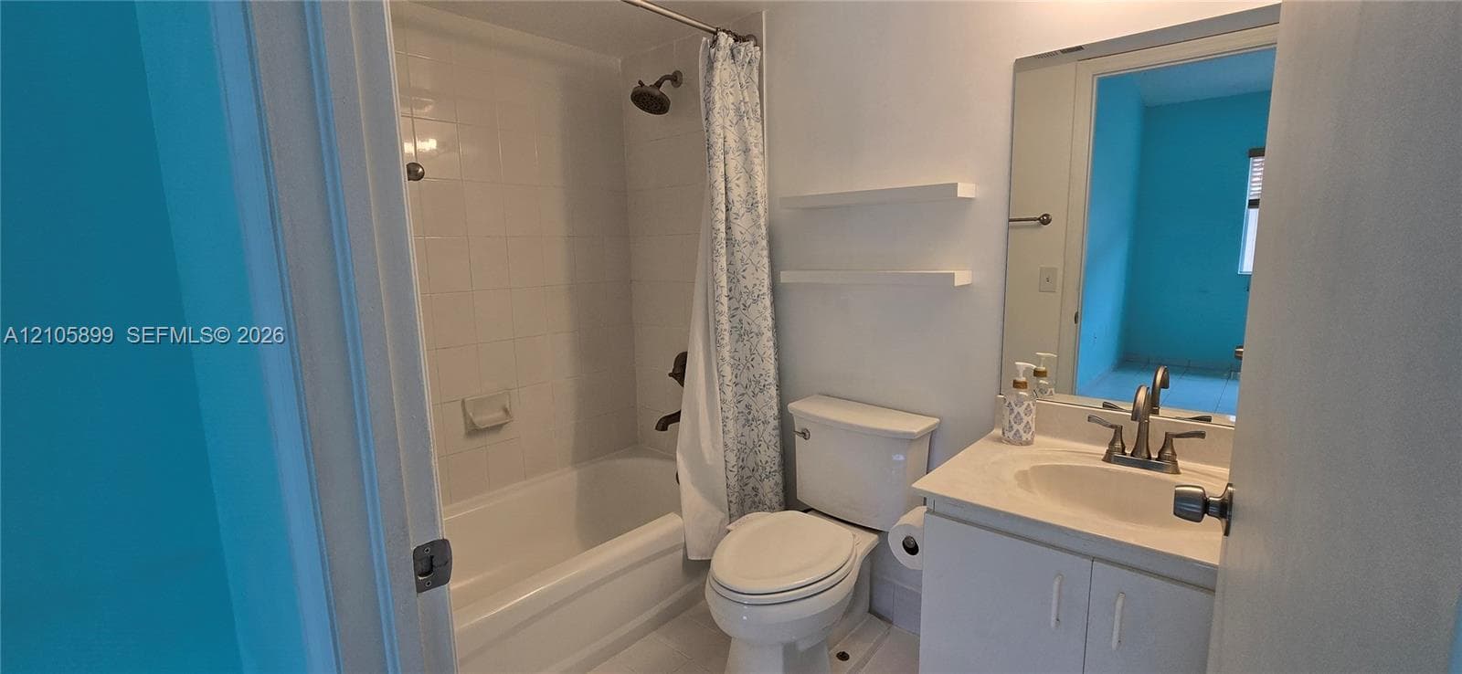 Full bathroom featuring a tub-shower combination with white wall tile, a vanity with a white countertop and oval sink, wall-mounted shelving, and a large frameless mirror