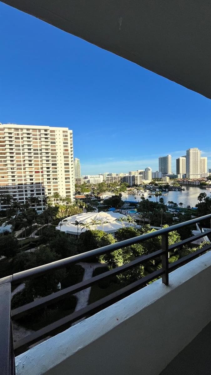 Covered balcony featuring a metal railing and panoramic scenery of the cityscape, waterway, and dense tree canopy