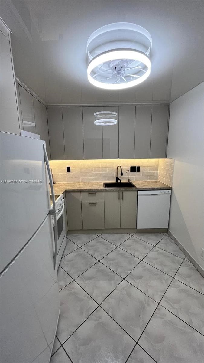 Kitchen featuring flat-panel cabinetry, light-toned tiled flooring, a brick-pattern backsplash, under-cabinet lighting, and a modern circular LED flush-mount fixture