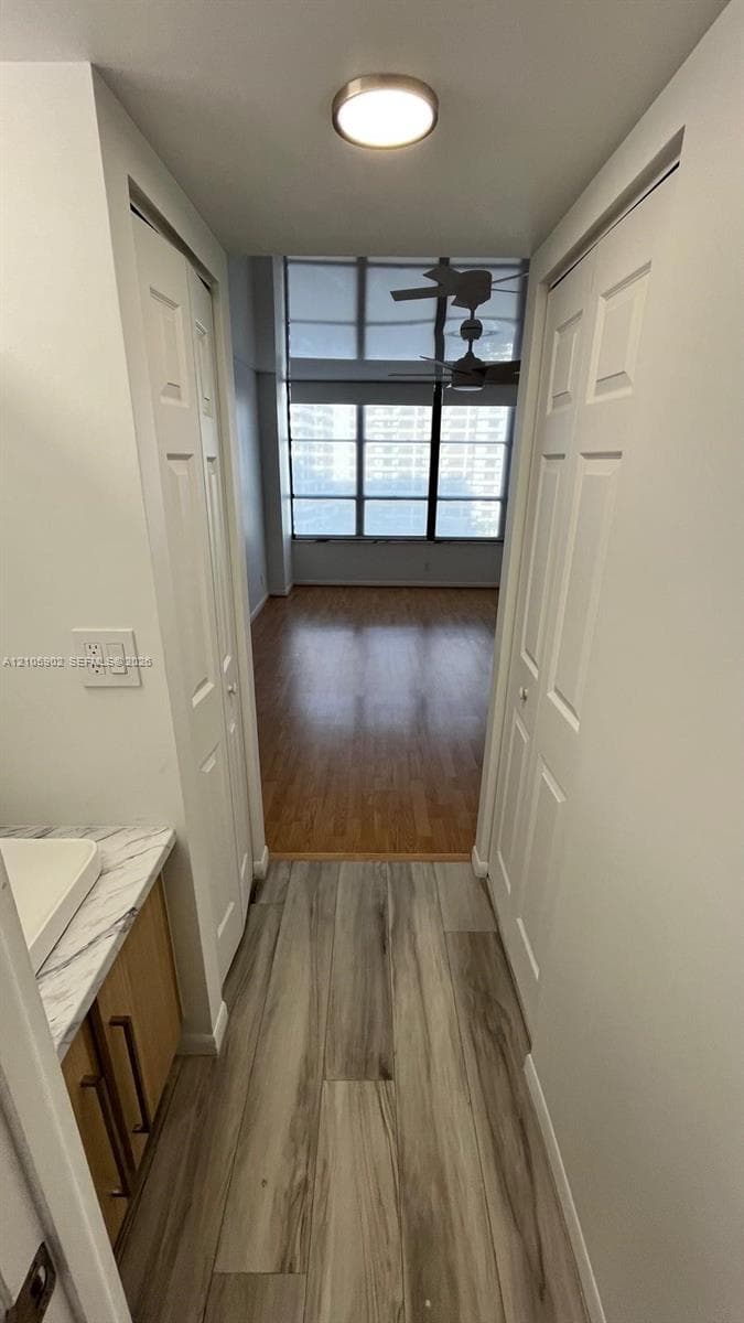Wood-finish flooring, vanity with stone-patterned countertop and vessel sink, dual bi-fold closet doors, and floor-to-ceiling windows