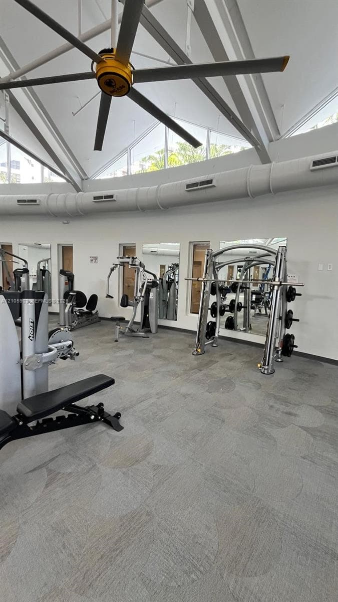 Vaulted ceiling with oversized industrial ceiling fan, clerestory windows, wall-to-wall mirrors, and resilient commercial-grade flooring