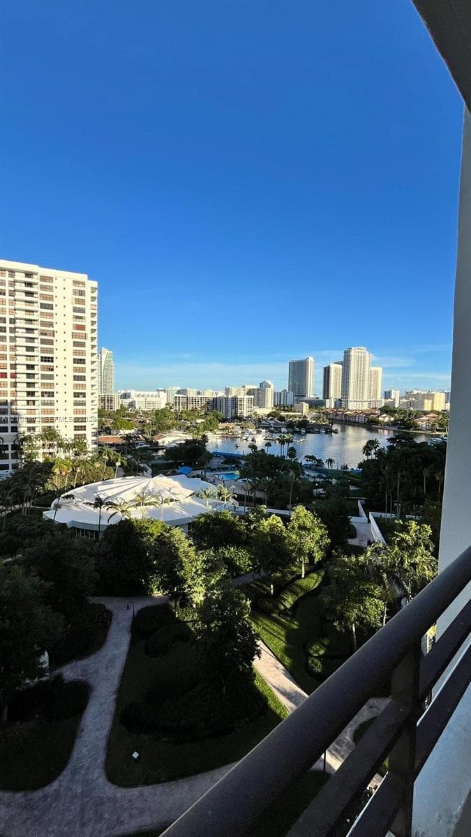 Elevated terrace with a metal railing overlooking a landscape of mature trees, paved pathways, and a waterfront cityscape