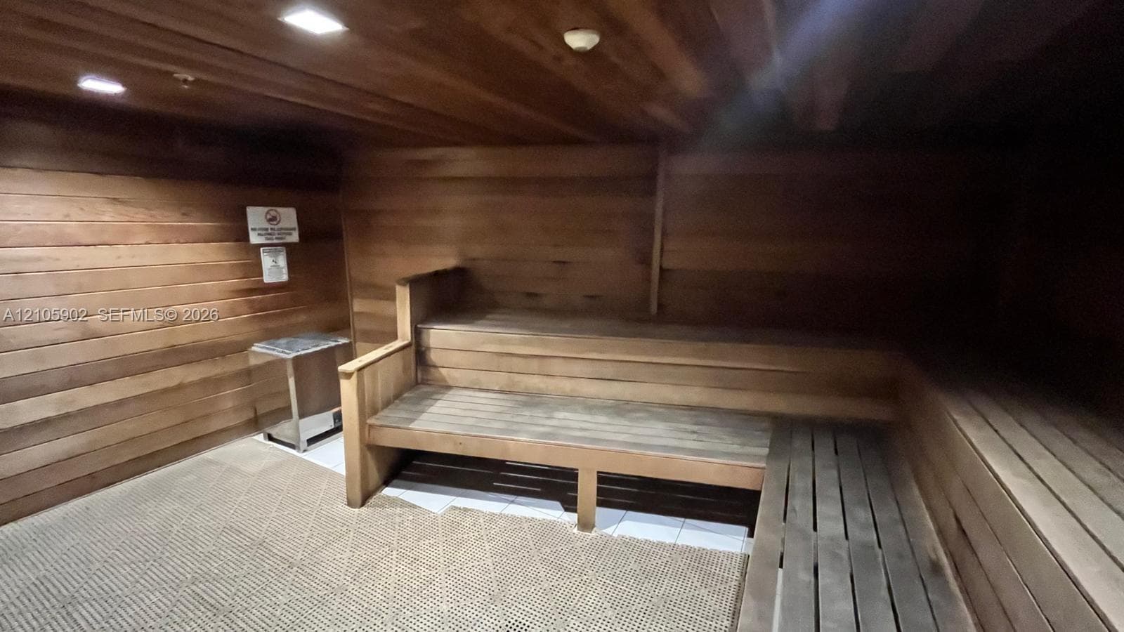 Sauna featuring tongue-and-groove wood paneling, multi-tiered built-in wood bench seating, integrated recessed lighting, and a metal heating unit