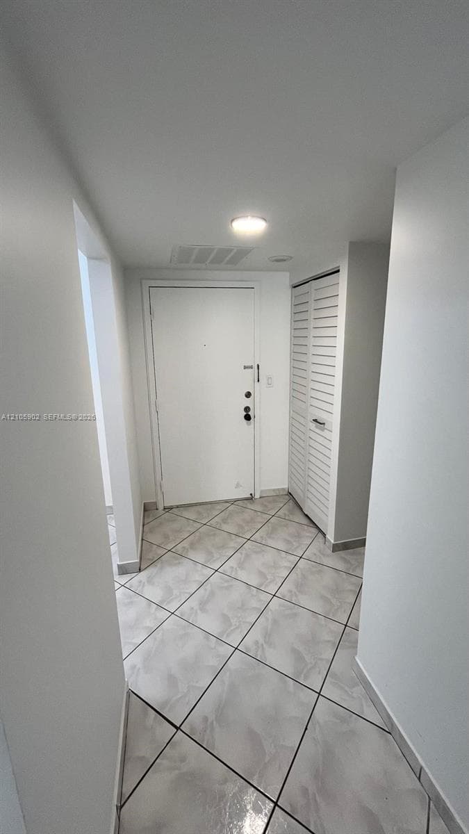 Entryway featuring large-format ceramic tile flooring, a white metal entry door with a deadbolt, and a built-in closet with louvered bi-fold doors