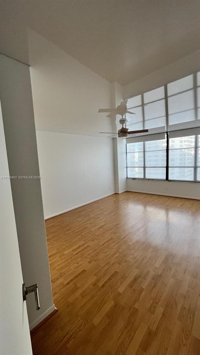 Expansive room featuring soaring ceilings, wood-finish flooring, floor-to-ceiling windows, and a ceiling-mounted fan