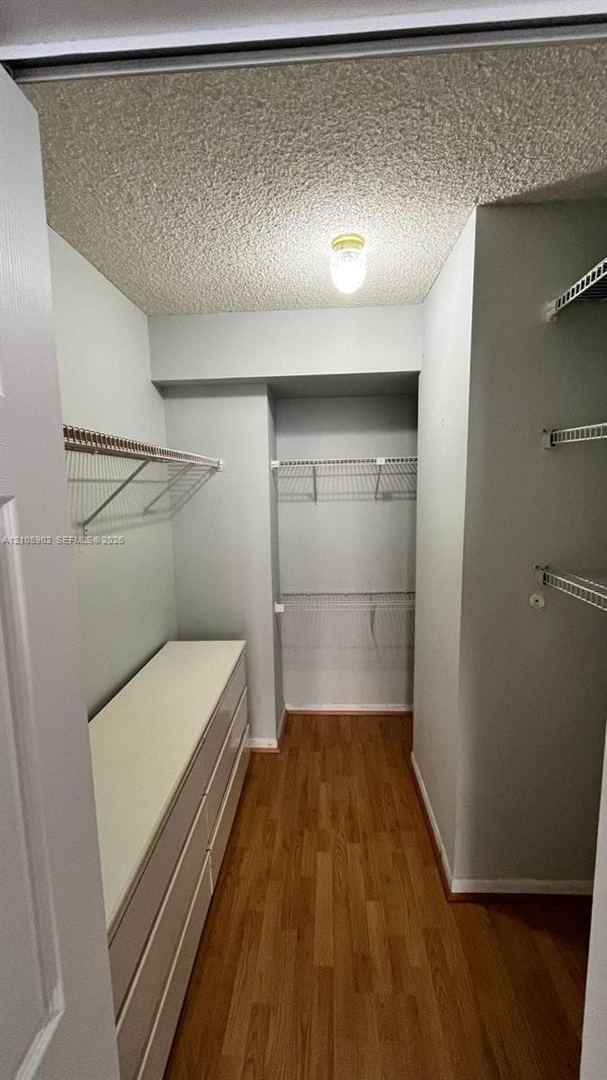 Walk-in storage space featuring wood-finish flooring, white built-in cabinetry, and multi-level wire shelving