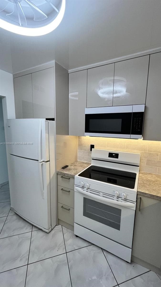 Kitchen featuring glossy, flat-panel cabinetry, stone-finish countertops, subway tile backsplash, and ceramic tile flooring
