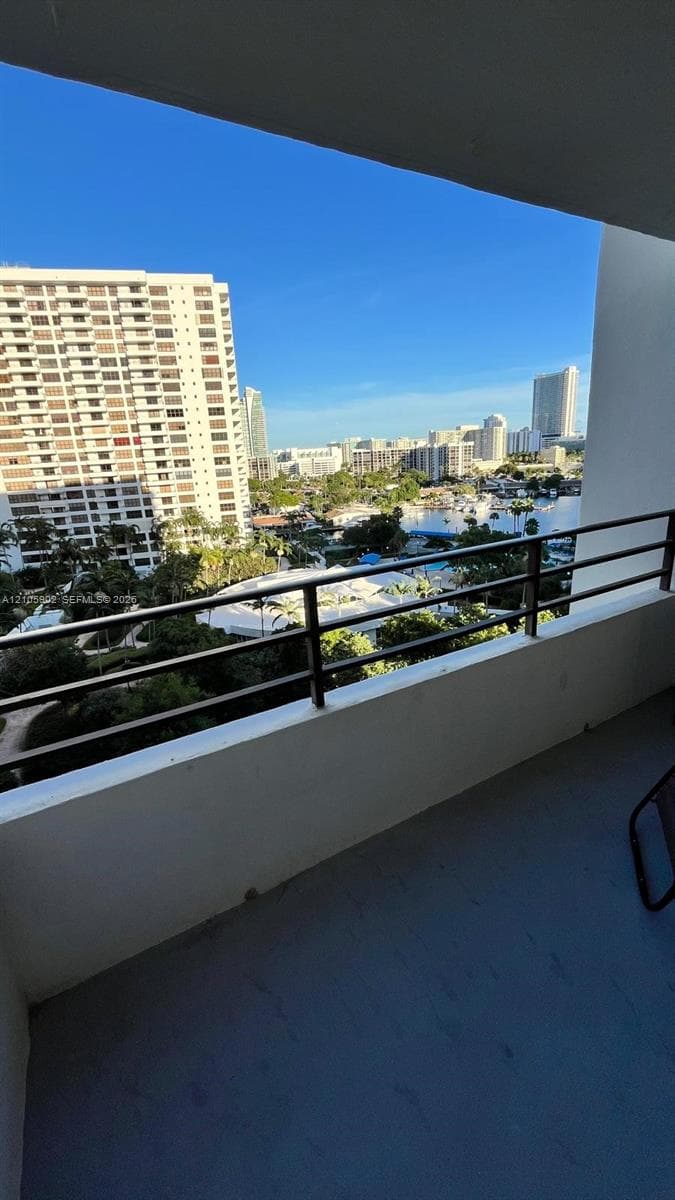 Covered balcony featuring concrete flooring and horizontal metal railings, showcasing an expansive cityscape and waterway panorama