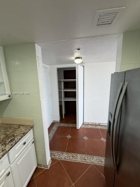 Kitchen area featuring patterned tile flooring with decorative border, white cabinetry, stone-finish countertops, built-in pantry with shelving, and flush-mount ceiling lighting