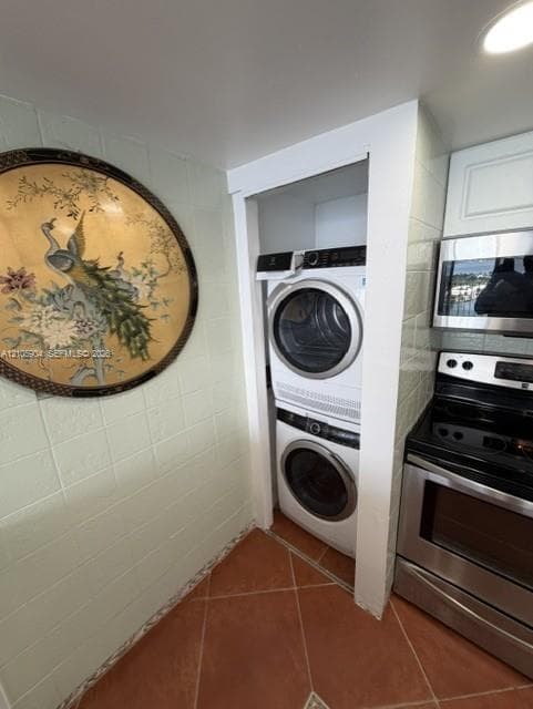 Stacked front-loading laundry appliances, stainless steel microwave, and stainless steel electric range, featuring tiled wall surfaces and terracotta-style floor tiling