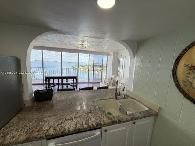 Kitchen featuring stone countertops, a dual-basin undermount sink, white cabinetry, and an arched pass-through opening to a balcony with water scenery