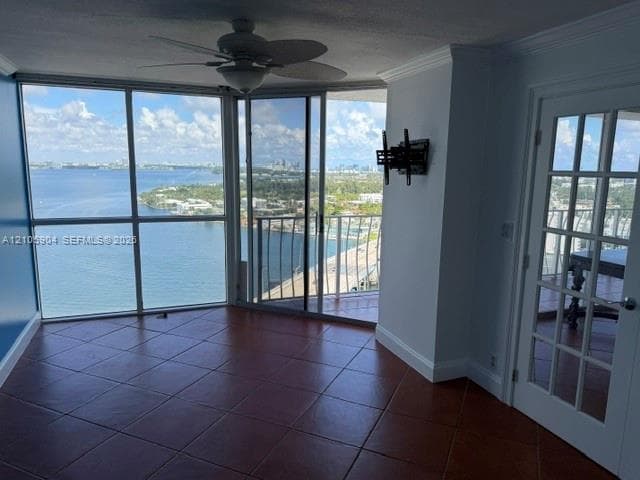 Floor-to-ceiling windows featuring panoramic water scenery, large-format tile flooring, sliding glass doors, a ceiling fan, and a French-style door