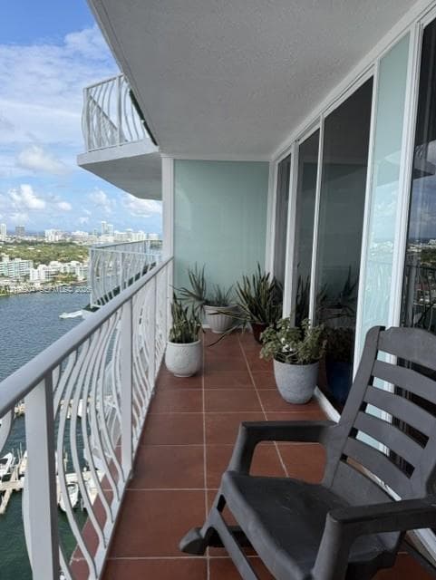 Covered balcony featuring tile flooring, white metal railings, and floor-to-ceiling glass sliding doors