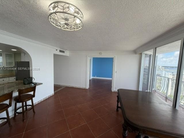 Open-concept interior featuring large-format tile flooring, a breakfast bar with stone-surface countertop, an ornate decorative flush-mount ceiling fixture, and floor-to-ceiling sliding glass doors opening to a balcony