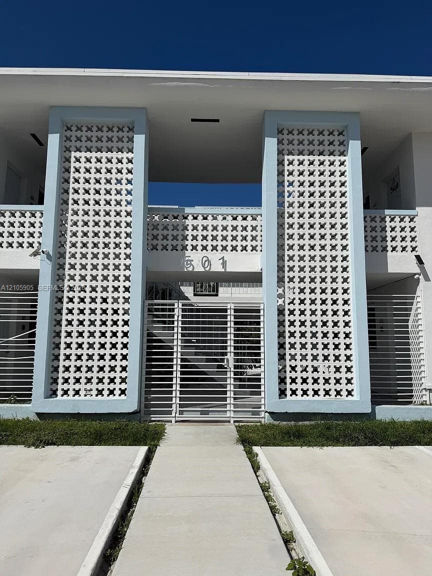 Mid-century modern exterior featuring decorative white concrete breeze blocks, two-story facade with structured columns, and a secure metal gate entryway
