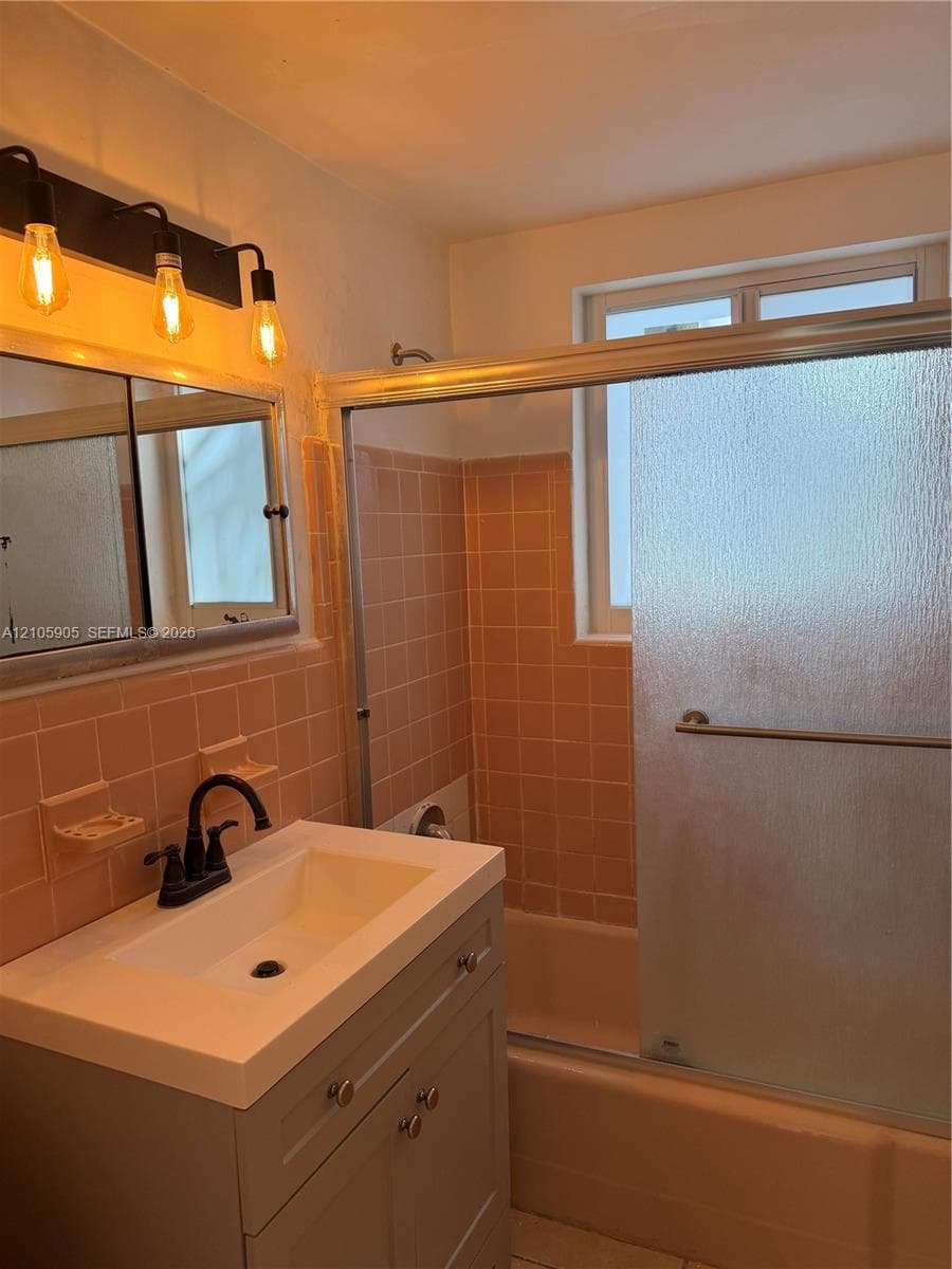 Bathroom featuring a vanity with integrated sink, matte black gooseneck faucet, tiled shower enclosure, sliding glass shower door, and three-bulb vanity light fixture