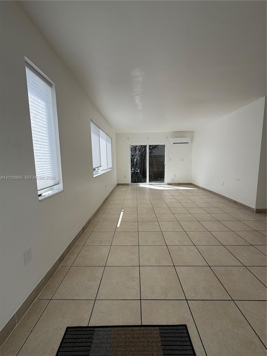 Neutral-toned ceramic tile flooring, sliding glass door, wall-mounted ductless climate control unit, and window treatments